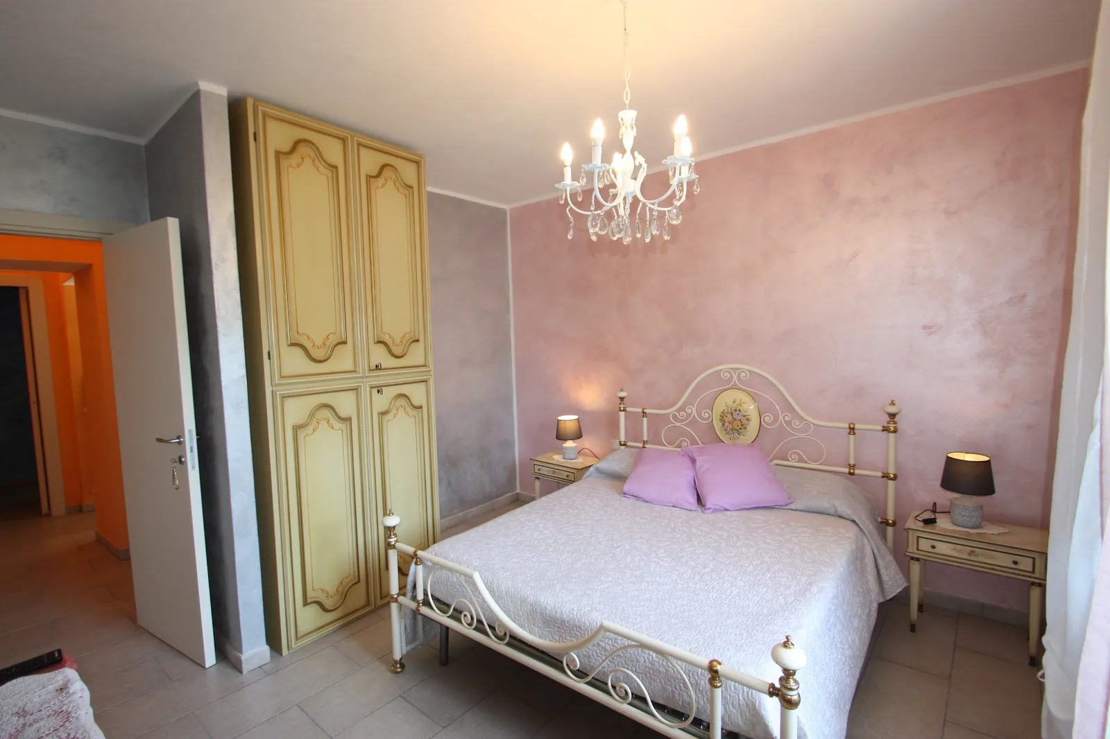 La camera rosa con il letto in ferro battuto e il lampadario