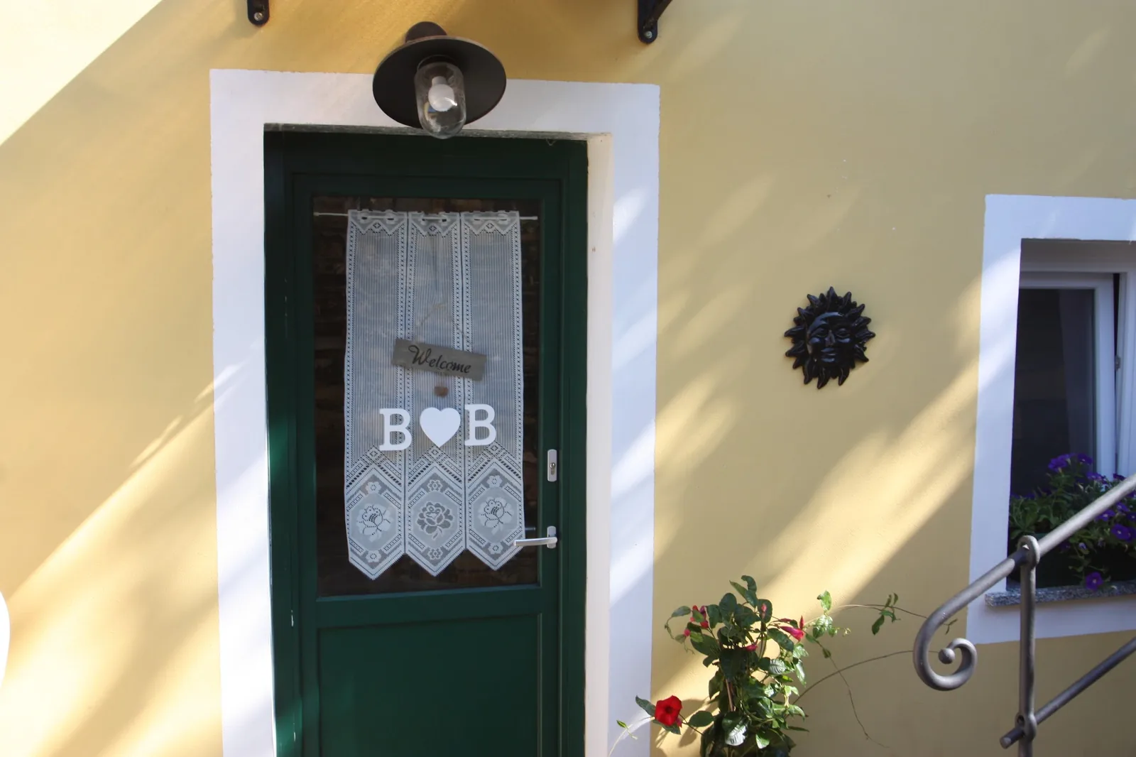 La porta d'ingresso verde con la tendina ricamata e i fiori